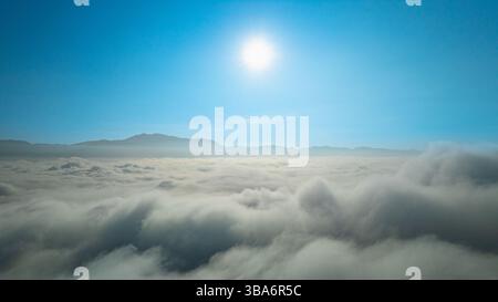 White fluffy clouds float above the mountaintops, forming a sea of ​​clouds. The blue sky in the morning, the sunlight shining on the fluffy clouds, i Stock Photo