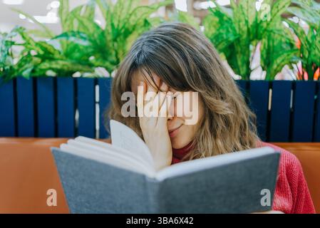 Exhausted student is covering her face with her hand while preparing for the exam, feeling stressed and overwhelmed by the amount of studying Stock Photo