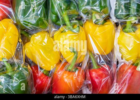 Plastic wrapped yellow, green and red bell peppers in a grocery shop Stock Photo