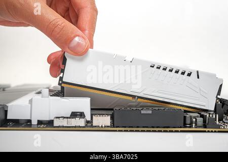 A person is carefully inserting a white DDR RAM module into a motherboard slot Stock Photo