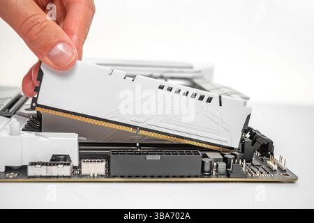A person is carefully inserting a white DDR RAM module into a motherboard slot Stock Photo