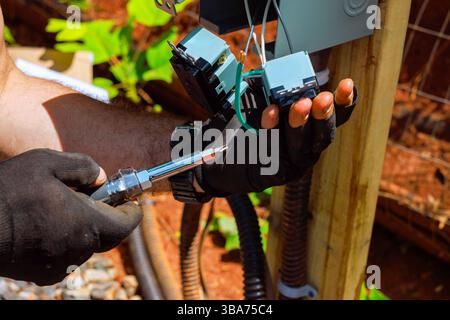 Tech fixes garden electrical outlets connections with tools, ensuring safety system functionality. Stock Photo