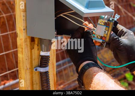 Technician works on outlets connecting wires to an electrical panel mounted outdoors in backyard. Stock Photo