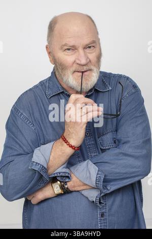 Portrait of an attractive grey-haired man in a denim shirt against a grey background. Bearded grandfather of the European type Stock Photo