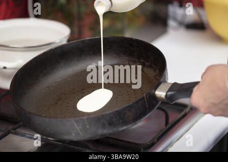 Pour the pancake batter into an old frying pan Stock Photo