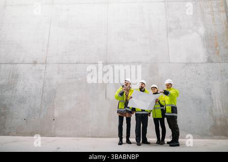 Team of engineers and construction workers reviewing blueprints, building site. Stock Photo