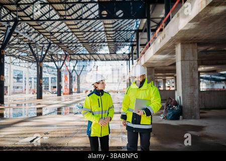 Engineers discussing construction plans using a tablet on site. Stock Photo
