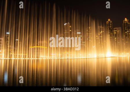 A stunning night view of a fountain display with illuminated water jets, set against a backdrop of tall city buildings. The scene reflects beautifully Stock Photo