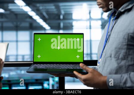 Employees in data center using isolated screen mockup laptop, integrating green technologies. IT experts in server room using chroma key notebook to implement sustainable energy solutions Stock Photo