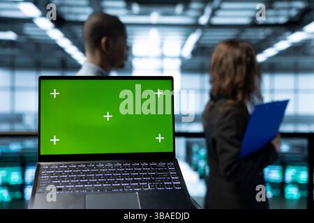Focus on isolated screen laptop in front of engineers in blurry background doing network virtualization. Close up of mockup chroma key notebook used by admins in server farm verifying settings Stock Photo