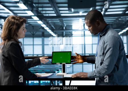 Software developers in data center using mockup tablet, observing analytics, reviewing equipment health. Server hub IT professionals talking, using chroma key device, adjusting system parameters Stock Photo
