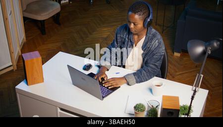 Woman arriving in apartment office, sitting down at desk, opening laptop to begin doing tasks. Teleworker starting job shift at home, preparing notebook device, logging in online, camera B Stock Photo