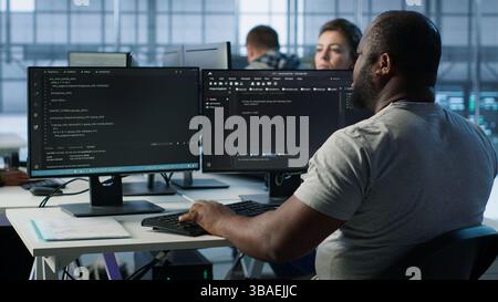 Admin programming in server room housing advanced equipment storing massive datasets. Developer typing code on PC to mend data center racks doing complex computational operations, camera A Stock Photo