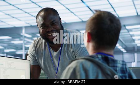 Engineer having fun with colleague at work in data center establishment, making jokes. Team of technicians making each other laugh, bonding in server room, doing fist bump gesture , camera A Stock Photo