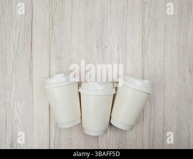 Three white paper coffee cups on light wooden background. Eco-friendly packaging. Top view. Flat lay. Stock Photo