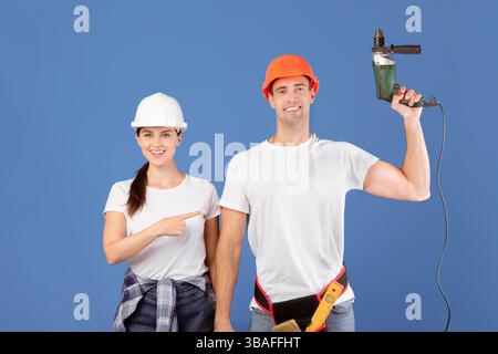 Repair Services. Happy Millennial Woman Pointing At Man With Drill In Hands Stock Photo