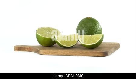 Featuring one whole lime, a halved lime, and two vibrant lime slices, all resting on a small wooden cutting board against a clean white background Stock Photo