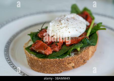 a delicious breakfast poached egg on a slice of ciabatta with spinach and pieces of red salted fish Stock Photo
