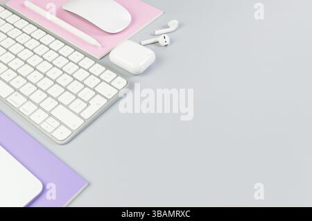 Top view of white keyboard, mouse, touchpad, earphones case, pen on grey background. Purple and pink notebooks, modern office, school. Stock Photo