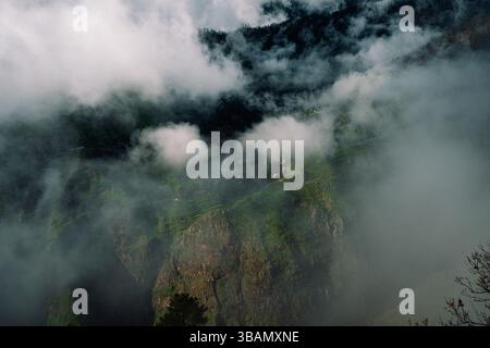 Misty mountain village nestled among green terraced slopes, shrouded in clouds Stock Photo