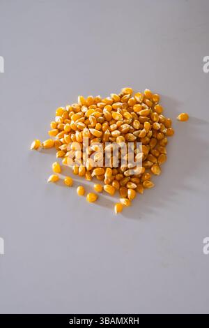 Short Description: A close-up of a small heap of yellow, dried popcorn kernels scattered on a smooth, pale grey surface. Stock Photo