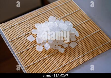 A close-up of a collection of clear, white rock sugar crystals piled on a light brown bamboo sushi rolling mat. Stock Photo