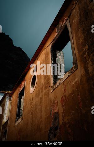 Abandoned building facade with broken windows and weathered walls against a dark sky Stock Photo