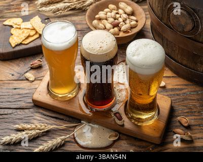 Three glasses of different beer types in beer glass holder and beer snacks on wooden background, top view. Stock Photo