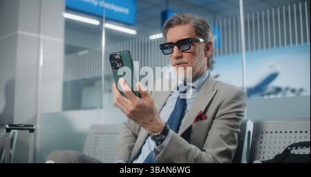 Airport Terminal: Successful Entrepreneur Talking to Investor on Smartphone by Video Chat, Drinking Coffee. Businessman Waiting for Flight in Departure Lounge, Going on Business Trip. Medium Close Up. Stock Photo
