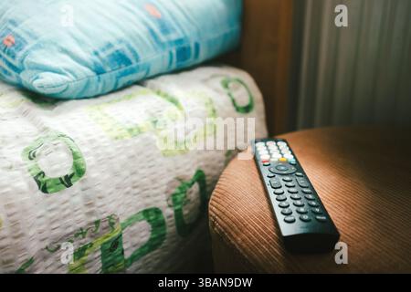 Remote control on the stool next to the bed in the room. Stock Photo