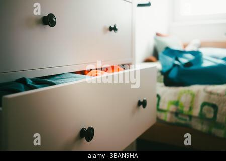 A half-open drawer with things, in the background the atmosphere of a room with a bed and a window. Stock Photo
