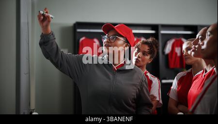 Women, coach and meeting with soccer team on whiteboard for match or game plan in locker room. Female people, coordinator or teaching with Stock Photo