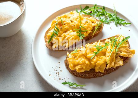 Scrambled Eggs on wholegrain bread toasts with arugula and cup of coffee close up. Healthy keto breakfast. Stock Photo