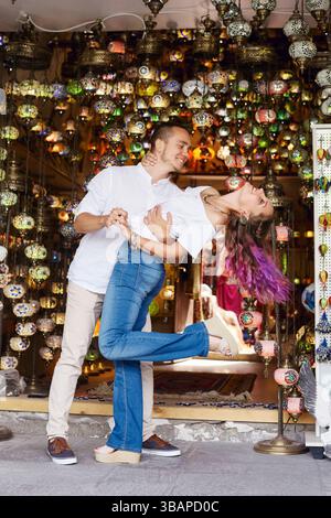 couple enjoys a playful dance in front of a lantern shop filled with colorful lights and decorations. atmosphere is lively, enhancing their joyful mom Stock Photo