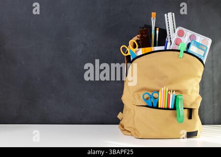 School backpack overflowing with Stationery Supplies on blackboard with copy space, ready for back to school season Stock Photo