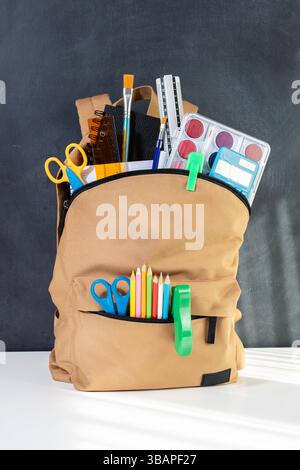 School backpack overflowing with Stationery Supplies on blackboard, ready for back to school season Stock Photo