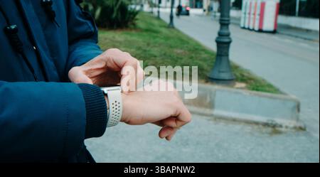 on a winter day, a man in a navy blue coat stands on the street, activating the GPS tracker on his smartwatch, ready for an outdoor walk, in a panoram Stock Photo