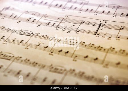 Close up of a vintage music score showing musical notes, symbols, and solfege syllables on aged paper Stock Photo