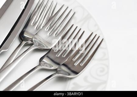 Silver forks on porcelain plate. Elegant table setting for formal dinner. Classic cutlery arrangement. Fine dining background. Stock Photo