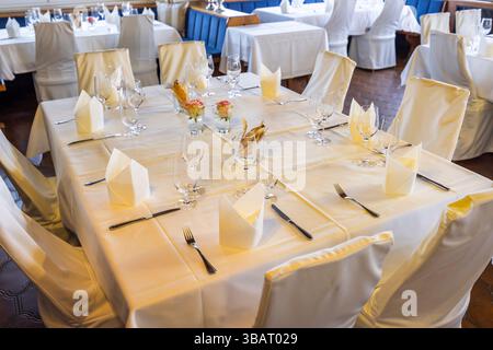 Elegant table setting waiting for guests in luxury restaurant with white tablecloth, napkins, cutlery, glasses and flowers Stock Photo