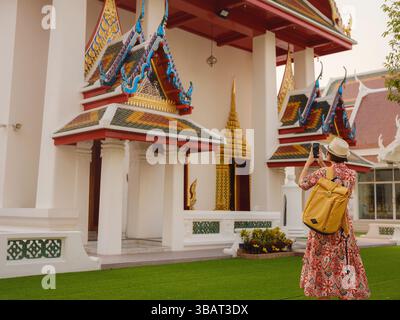 Woman Exploring Colorful Streets Near Buddhist Temples in Bangkok. Female traveler strolling through charming streets of Bangkok, surrounded by tradit Stock Photo