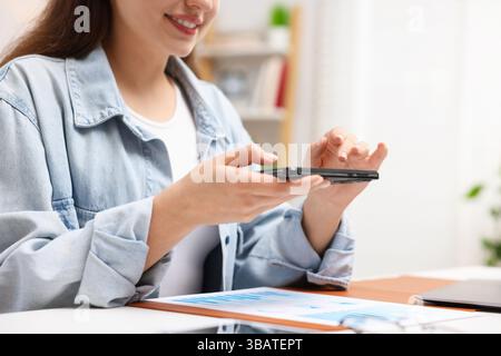 Woman taking photo of document using scanning app on smartphone at desk in office, closeup Stock Photo