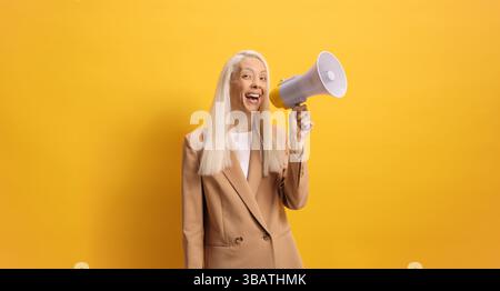 Woman speaking with a megaphone against yellow background Stock Photo