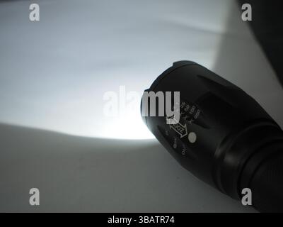 Close-up image of a black tactical flashlight. The scene symbolizes preparedness and reliance on alternative lighting during a power outage. Stock Photo