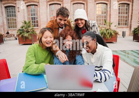 A cheerful group of students is engaged in a collaborative project, sharing ideas and laughter while gathered around a laptop, showcasing friendship Stock Photo