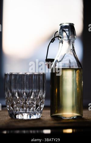 An empty rocks glass on a table next to a flip-top bottle of mead Stock Photo