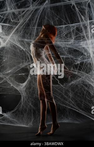 Red-haired woman trapped in a delicate net of web during a creative dance Stock Photo