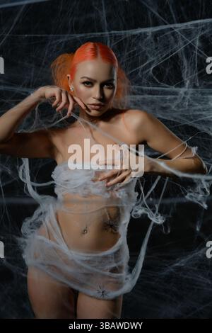 Red-haired woman entangled in a delicate net trap amidst a haunting web backdrop Stock Photo
