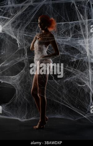 Red-haired woman trapped in intricate web display during an artistic showcase Stock Photo