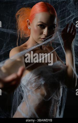 Red-haired woman ensnared in a delicate net trap amidst a dark background Stock Photo